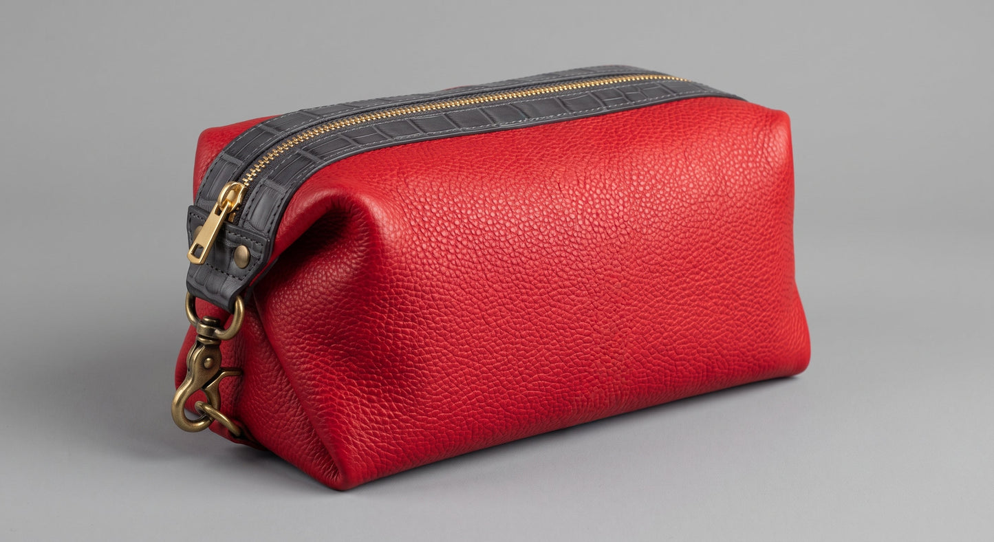 A close-up shot of the travel dopp kit made from smooth brown Italian leather, featuring distinct black alligator leather accents on the side trim and zipper pull tabs.
