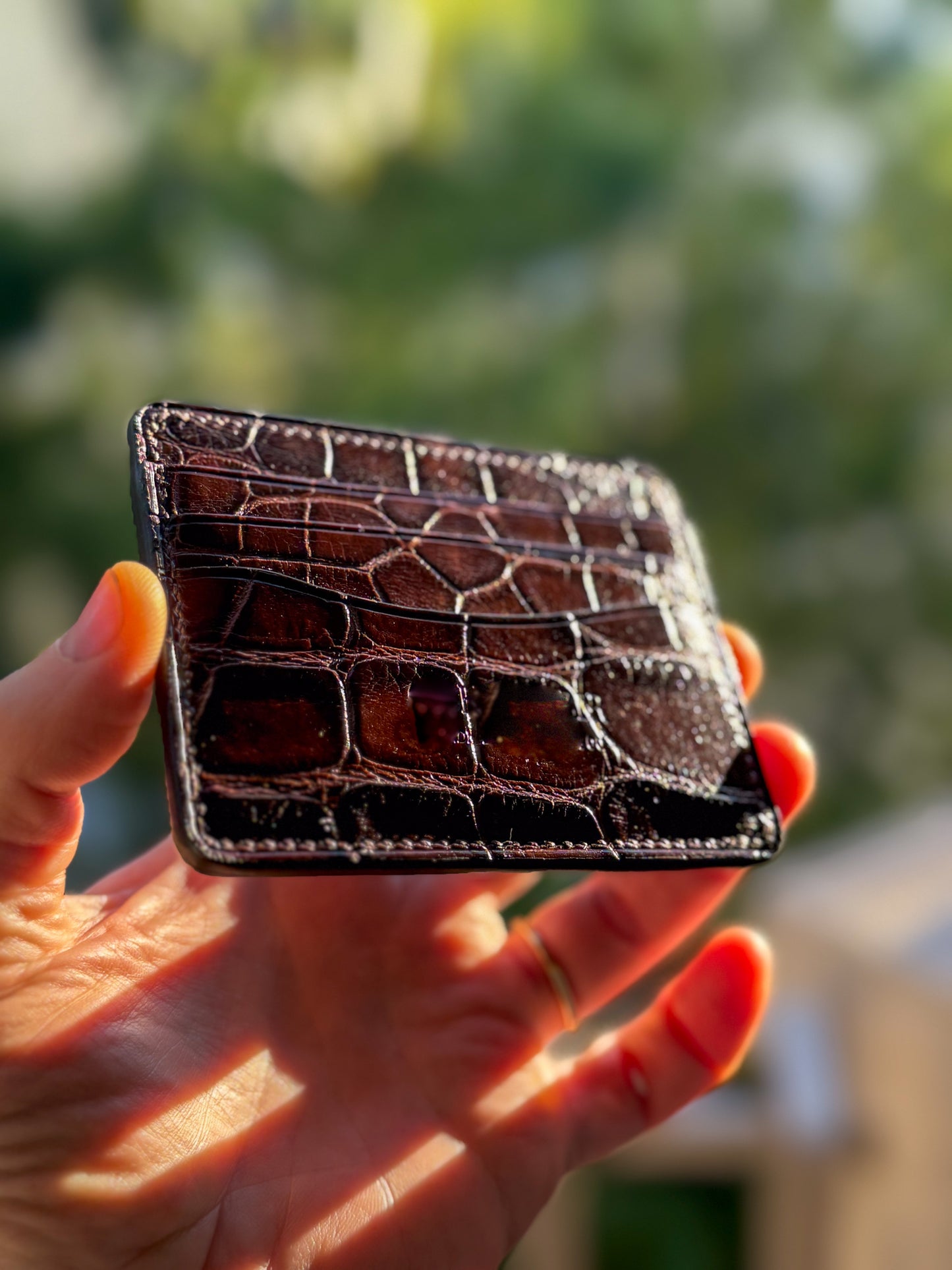 
                  
                    Front view of a slim dark brown alligator leather card holder showing natural scale patterns and card slots.
                  
                
