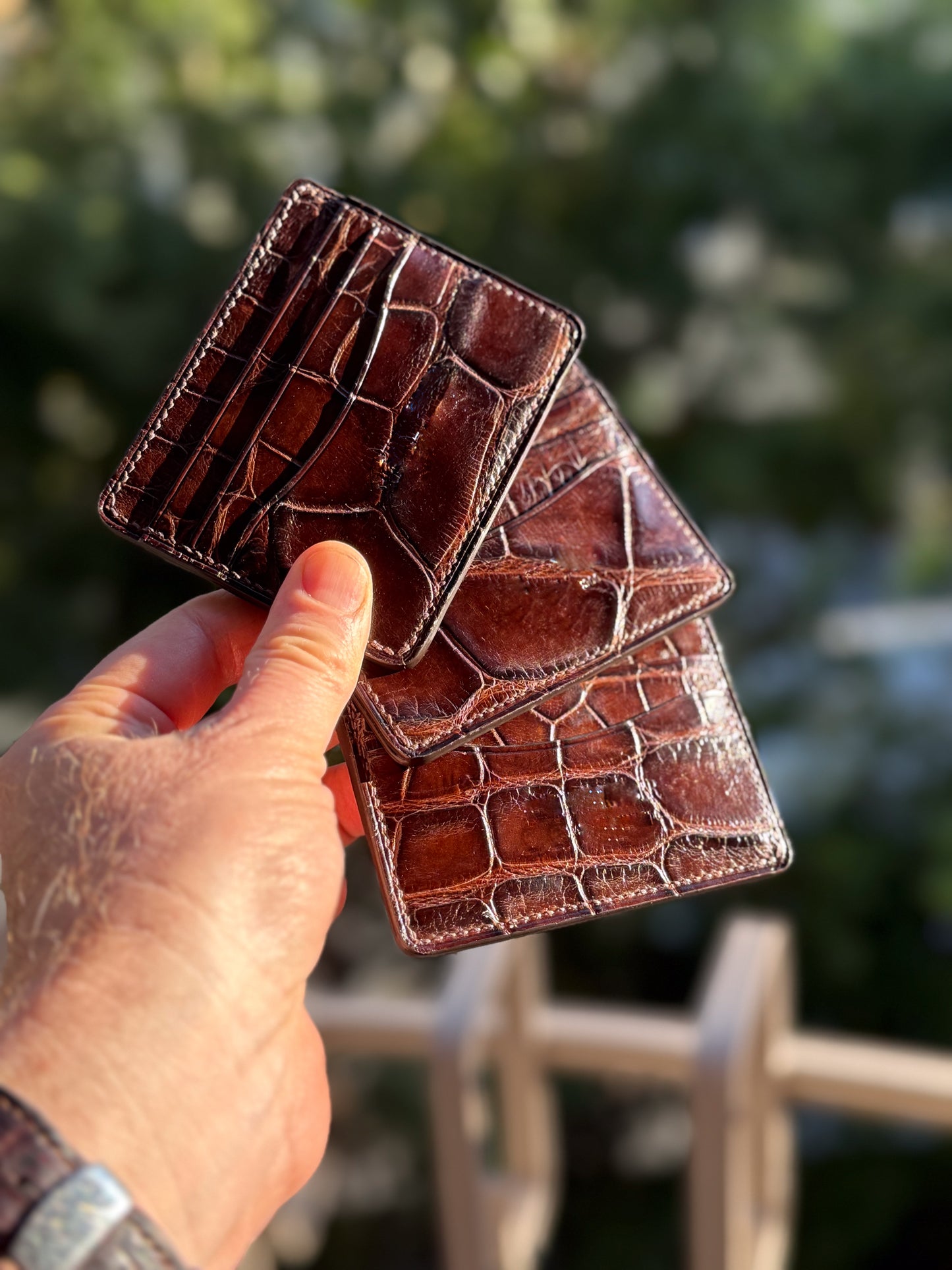 
                  
                    Hand holding a dark brown alligator leather card holder to demonstrate real-world size and compact fit.
                  
                