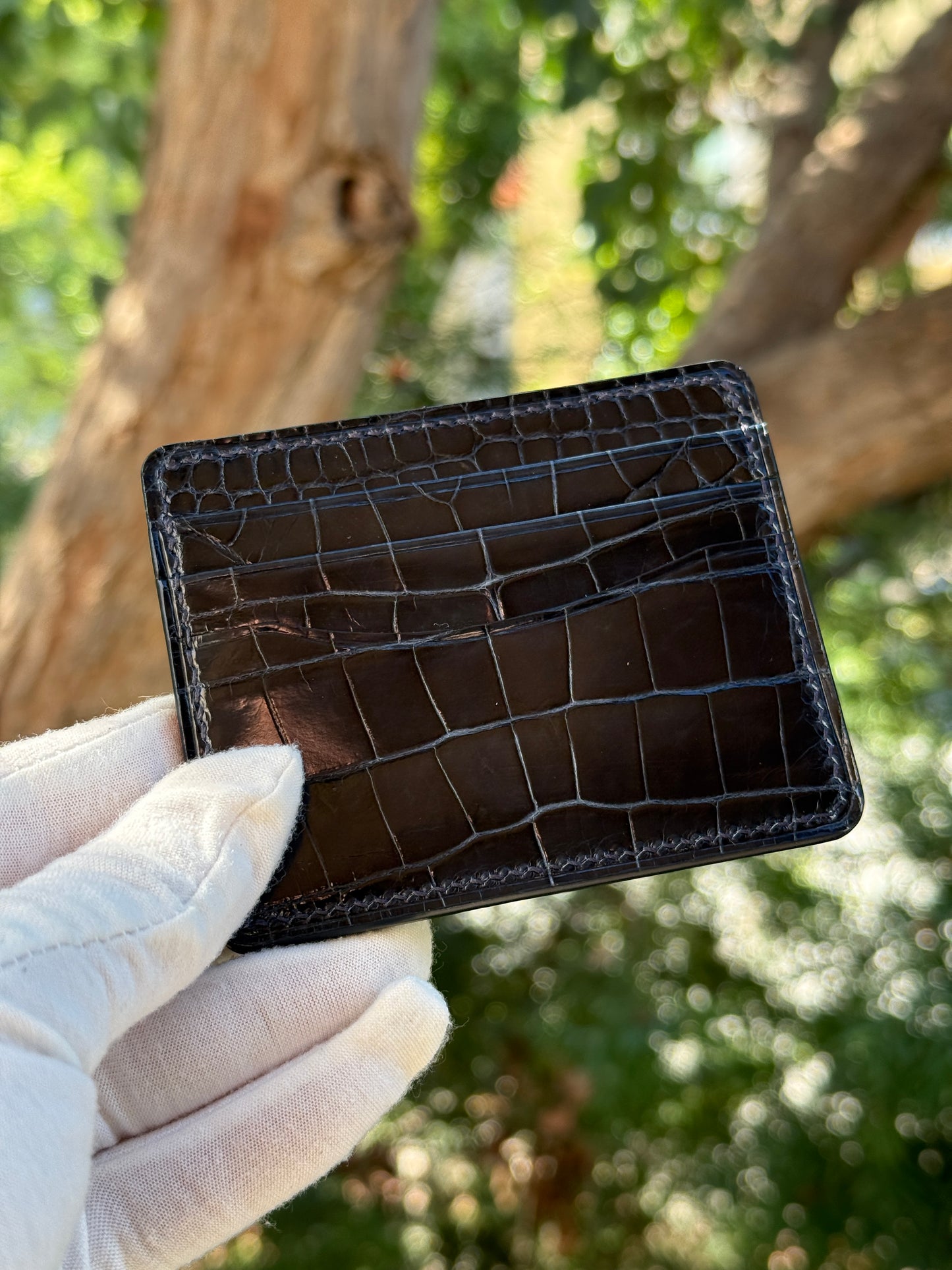 
                  
                    Hand holding a slim navy glazed alligator card wallet to show real-world scale and compact size.
                  
                