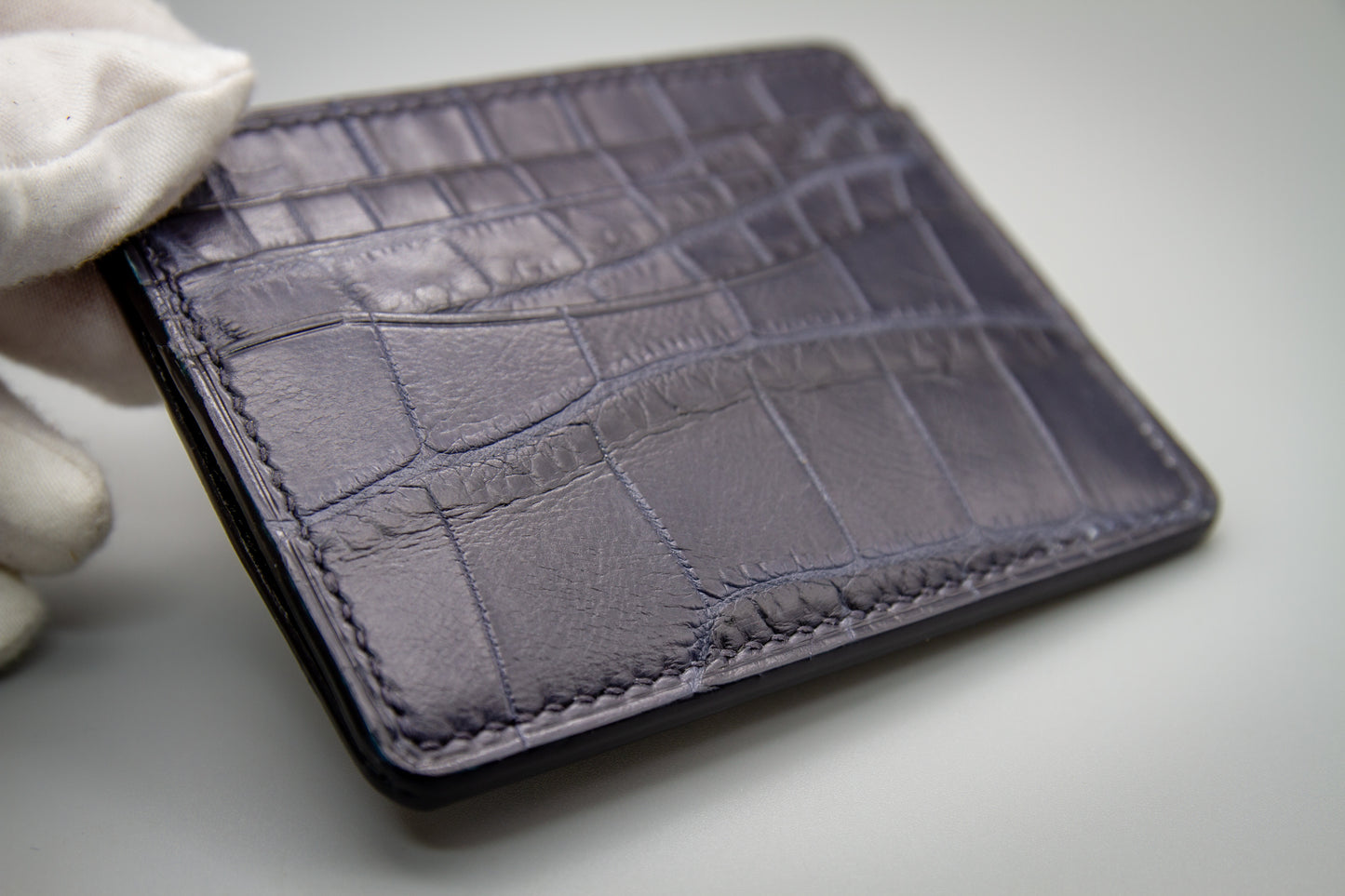 
                  
                    Three-quarter angle of a matte navy alligator card holder showing its slim profile and layered card pockets.
                  
                