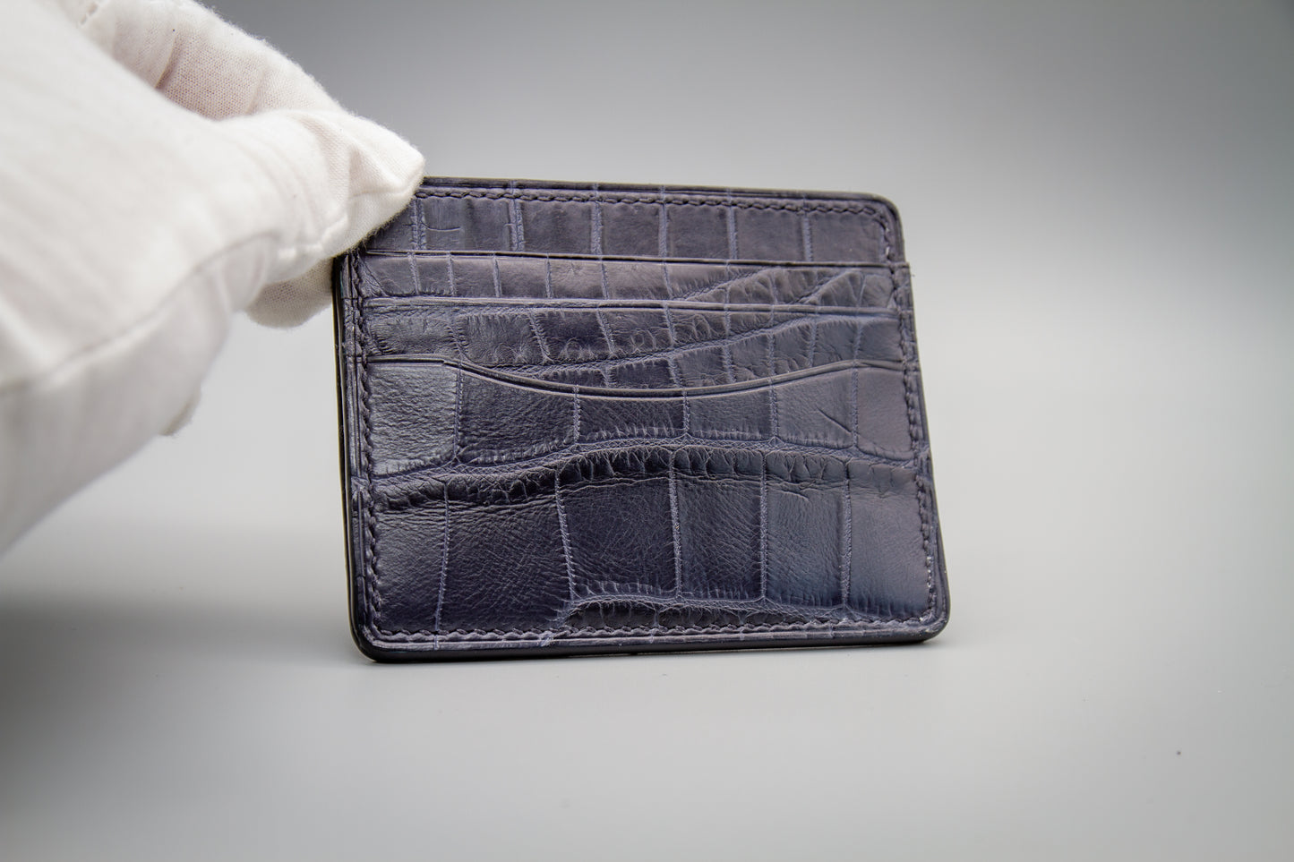 
                  
                    Front view of a slim matte navy alligator leather card holder showing low-glare scale patterns and card slots.
                  
                