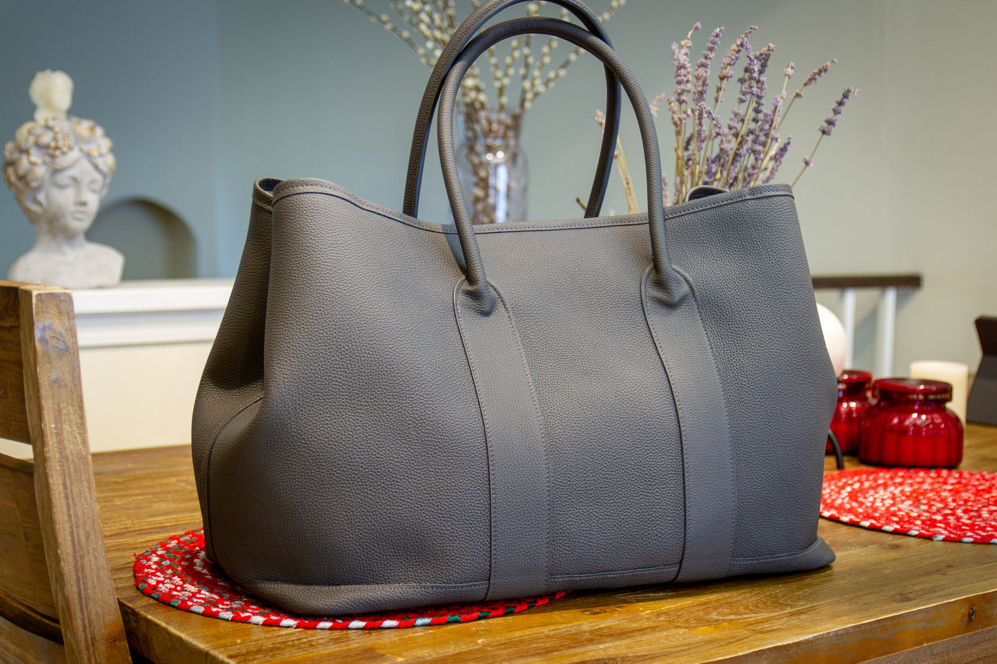 
                  
                    Front angled view of a handcrafted large gray Togo leather voyager tote bag with rolled leather handles, sitting on a wooden table.
                  
                