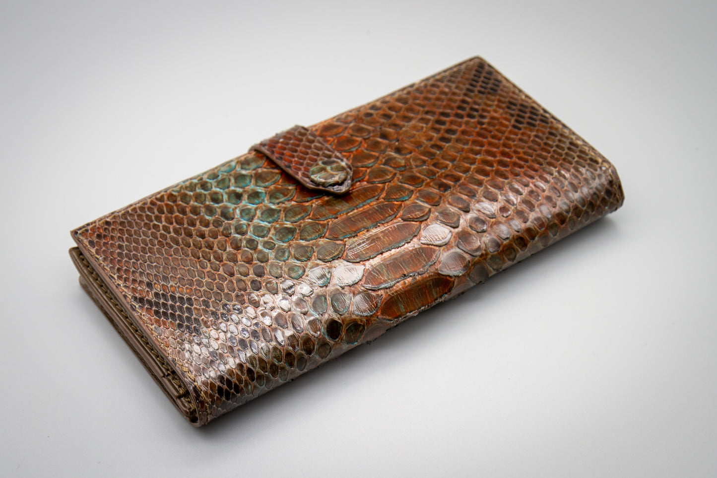 Closed women's long wallet in hand-painted python leather showing natural scale texture and strap closure.