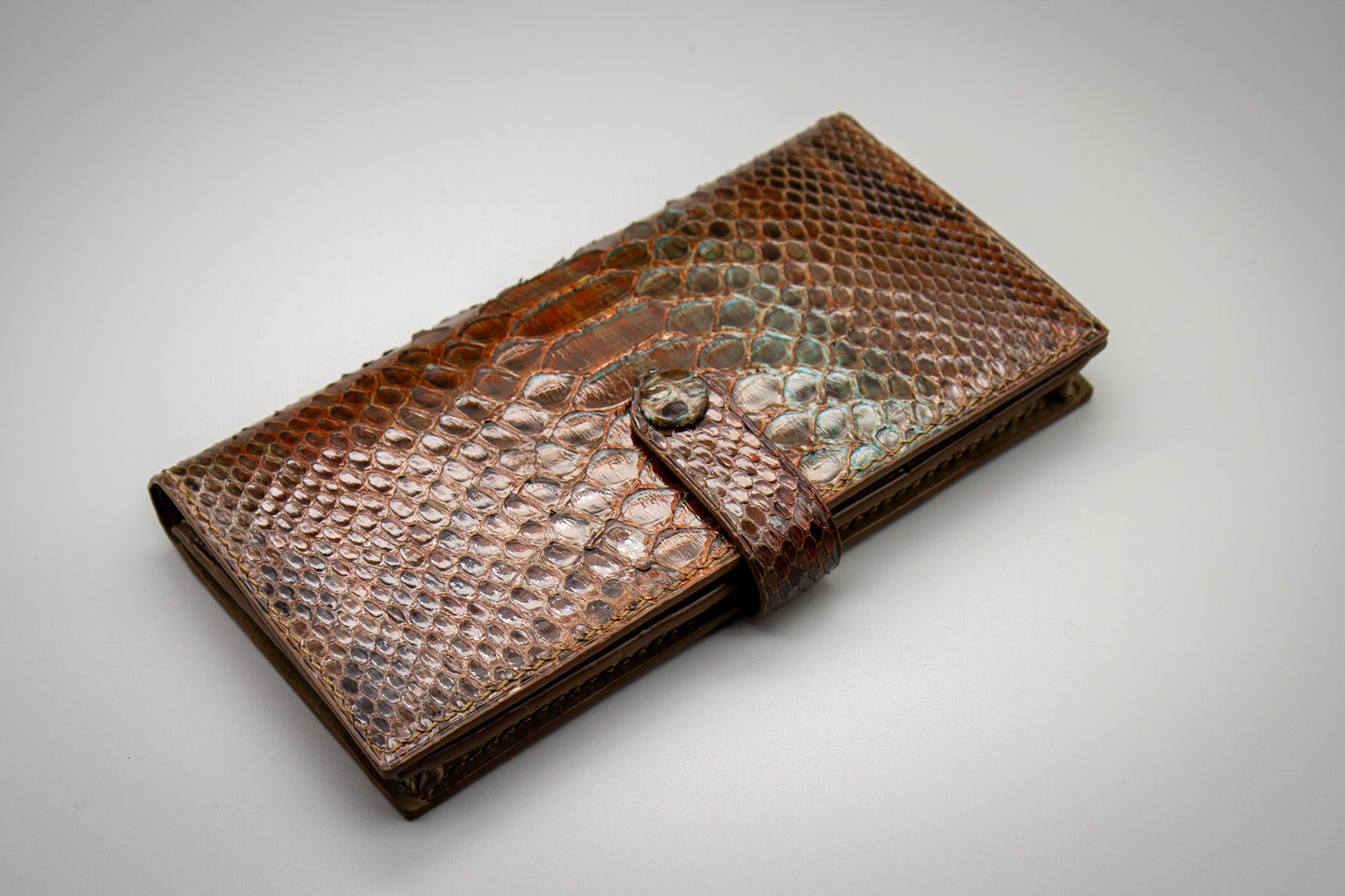 
                  
                    Flat lay view of a hand-painted python long wallet styled on a plain surface alongside daily carry accessories.
                  
                