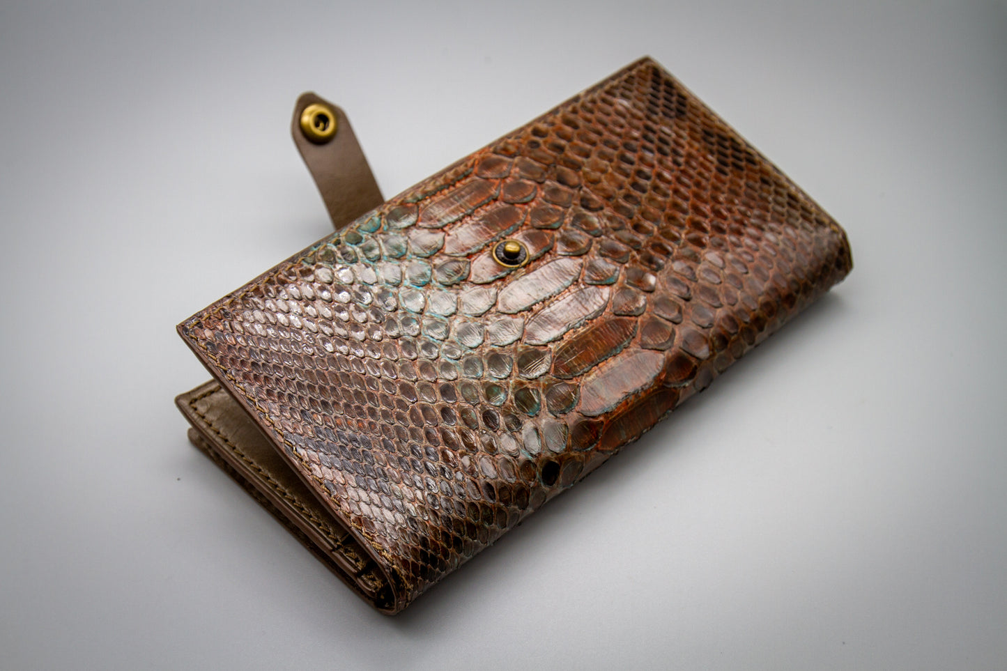 
                  
                    Half-open view of the women's long wallet with the snap strap released, showing interior leather lining.
                  
                