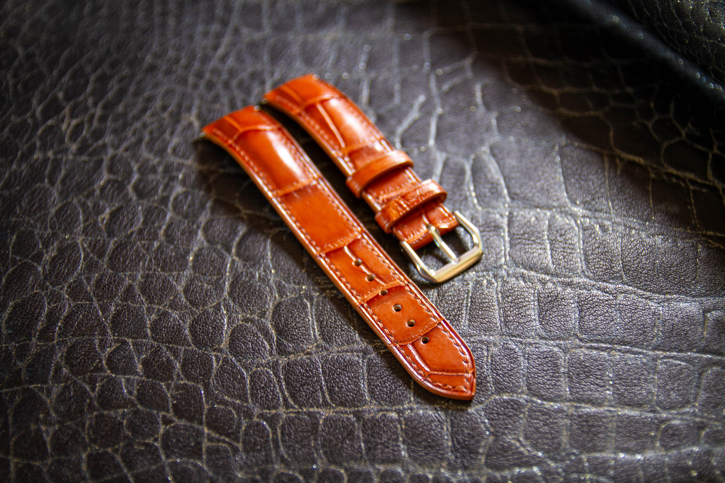 
                  
                    Angled perspective of bespoke cognac alligator leather watch strap set against dark croc-embossed backdrop
                  
                